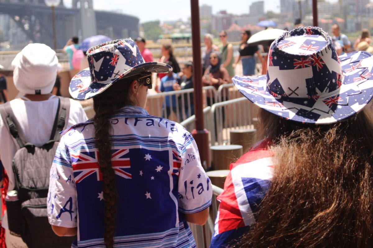 People in Australian attire celebrating at Sydney Harbour under bright sunlight.